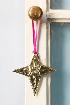 a gold star ornament hanging from a white door with a pink ribbon around it