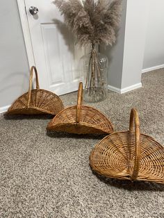 three wicker baskets sitting on the floor next to a vase with feathers in it