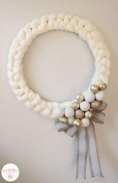 a white wreath with gold and silver ornaments hanging on the wall next to a gray ribbon