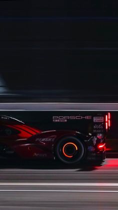 a red sports car driving down a race track at night with its headlights turned on