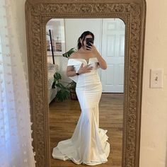 a woman taking a selfie in front of a mirror wearing a white gown and holding a camera