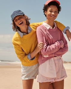 two young women standing on the beach with their arms around each other and smiling at the camera