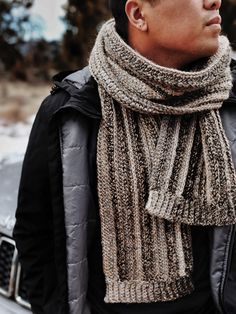 a man standing in front of a car wearing a knitted scarf over his neck