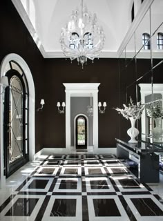 an elegant foyer with chandelier, mirror and black and white tile flooring