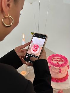 a woman taking a photo of a pink cake on her cell phone with candles in the background