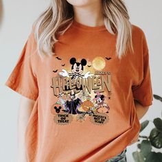 a woman wearing an orange halloween t - shirt with mickey mouse and friends on it