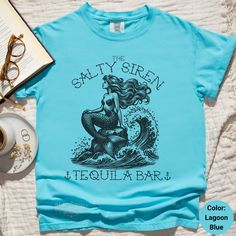 the salty siren tequila bar t - shirt sits next to a cup of coffee and eyeglasses