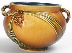 a brown vase with an acorn decoration on the rim and handles, sitting on a white surface