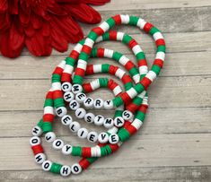 a red and green beaded necklace next to a flower on a wooden surface with words written in white letters