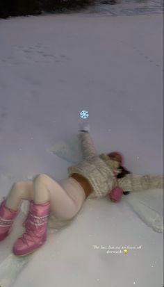 a woman laying in the snow wearing pink boots