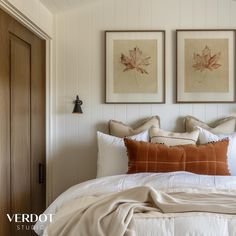 a bed with two framed pictures on the wall above it and an orange throw pillow