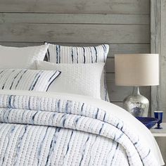 a bed with white and blue striped comforter next to a lamp on a night stand