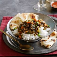 a plate with rice, meat and vegetables on it next to two silver spoons