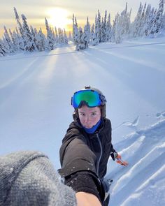 a person in ski gear and goggles pointing at the camera with snow covered trees in the background