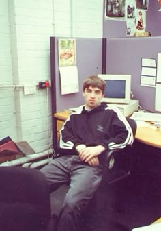 a young man sitting in an office chair next to a desk with computers on it