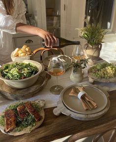 a woman pouring wine into a glass on top of a table filled with plates and bowls