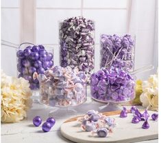 purple and white candies are arranged in glass vases on a table with flowers