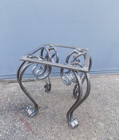 a metal table sitting on top of a cement ground next to a blue wall,