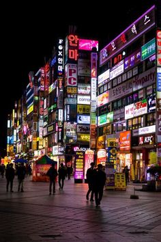 many people are walking down the street in front of some buildings with neon signs on them