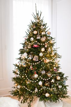 a christmas tree with ornaments on it in a room next to a white rug and window