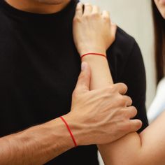 a man and woman with red bracelets on their wrists looking at each other's wrist