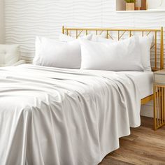 a bed with white sheets and pillows next to a gold headboard on a wooden floor