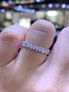 a person's hand with a diamond ring on top of their finger, in front of a blurry background