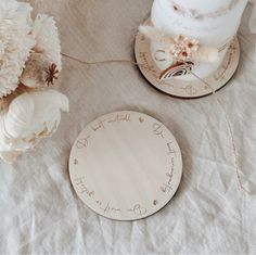 two wooden plates with writing on them sitting on a table next to flowers and a cake