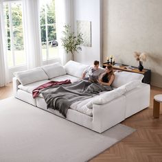 a man and woman sitting on top of a white couch in a living room next to each other