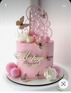 a pink cake with butterflies and flowers on it's top is sitting on a table