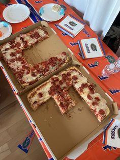 two pizzas cut into eight pieces on an orange table with plates and utensils