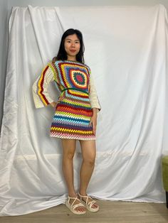 a woman standing in front of a white backdrop wearing a multicolored crochet dress