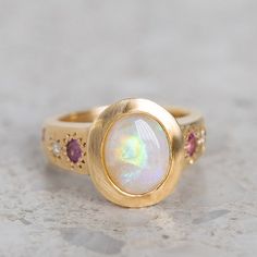 Our Sun Punch Ring has been set with a Crystal Opal from Coober Pedy and bead set with Pink Sapphires, G/VS White Diamonds and Salt & Pepper Diamonds in the band. Opal measures approx. 10 x 8mm. There are a total of three birlliant cut pink sapphires and four brilliant cut diamonds. Band width tapers from approx. 6mm to 3.4mm at the back of the band. Gold weight approx. 11g in 14ct, 12.6g in 18ct. This ring is pictured with a matte finish. For a polished finish please leave a note at the checkout. Please note, we will match the opal as close to the image as possible. Each opal is unique and may vary in appearance and colour from what is depicted on the site. Opal Signet Ring, Opal Wedding Ring, Pink Sapphire Ring, Coober Pedy, Crystal Opal, Bead Set, Jewelry Lookbook, Salt And Pepper Diamond, Opal Crystal