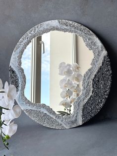 there is a mirror that has flowers in front of it and a vase with white flowers next to it