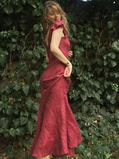 a woman in a red dress standing next to some bushes