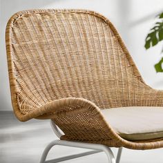 a wicker chair with a cushion on top of it and a potted plant in the background