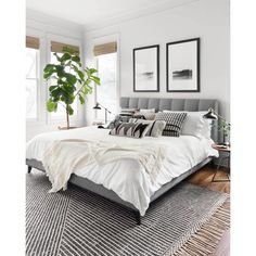 a bed with white sheets and pillows in a bedroom next to two plants on the floor