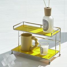 a yellow shelf with two cups and a bottle on it