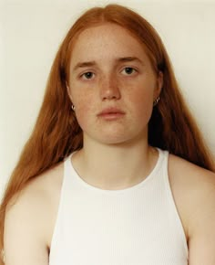 a young woman with freckles on her face is posing for the camera while wearing a white tank top