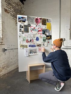 a man sitting on the ground in front of a white board covered with stickers