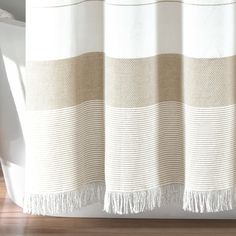 a white and beige striped shower curtain next to a bathtub in a bathroom with wood flooring