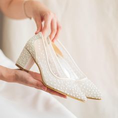 a woman holding a pair of white shoes with pearls on the toes and heels are being held by her hand