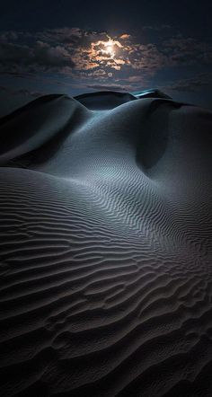 the moon shines brightly in the night sky over sand dunes, with dark clouds