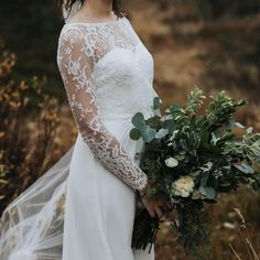 a woman wearing a wedding dress holding a bouquet of flowers and greenery in her hands