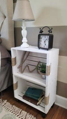 a small white shelf with a clock on top of it next to a lamp and books