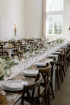 a long table is set with white plates and place settings for an elegant dinner party