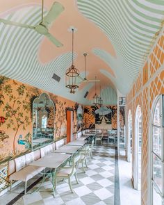 the dining room is decorated in an art deco style with white and orange walls, checkered flooring, arched windows, and chandeliers hanging from ceiling fans