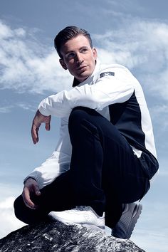 a man in white shirt and black pants sitting on rock with his hand on his hip