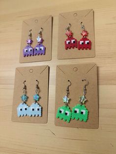 four earrings with different designs on them sitting on top of a wooden table next to each other