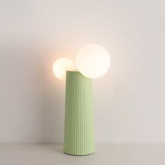 a green vase sitting on top of a table next to a white wall and two lights